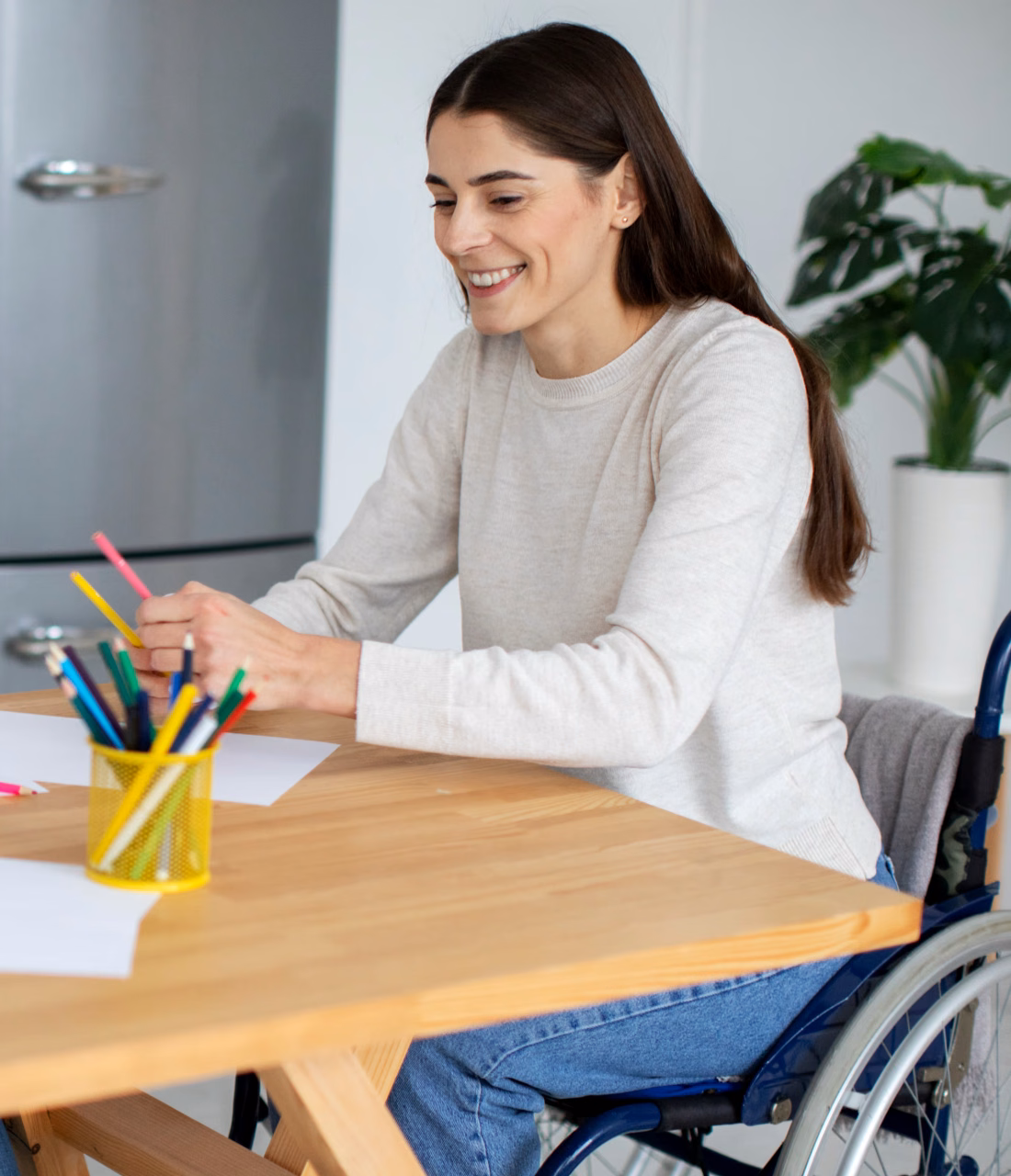 A woman using a wheelchair chooses coloured pencils at a kitchen table.